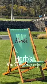 Here are a few options for your SEO alt text, depending on what is most prominent in the image:

**Option 1 (Focus on the branding/location):**
"Herb’s cafe branding with healthy smoothies and food inside the Old Course Hotel in St Andrews, Scotland."

**Option 2 (Focus on the food/drink):**
"Selection of health-focused smoothies, vitality pots, and coffee at Herb’s cafe in St Andrews."

**Option 3 (Short & descriptive):**
"Healthy smoothie, salad, and coffee served at the new Herb’s cafe inside the historic Old Course Hotel, St Andrews."

**SEO Tip:** I included the name of the cafe ("Herb's"), the location ("St Andrews"), and the "Old Course Hotel," as these are the high-value keywords people are likely to search for.