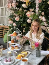 A beautifully composed, high-quality photograph capturing an afternoon tea service. The subject is well-lit and positioned against a vibrant floral backdrop, creating an inviting and aspirational atmosphere typical of a premium hospitality experience.