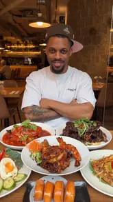 A food review video featuring a creator visiting Sentosa, a Singaporean and Malaysian restaurant in London. The video highlights specific dishes like crab, prawns, chicken satay, and nasi goreng, showing both the finished plates and the cooking process in the kitchen.