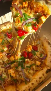 A fast-paced montage showcasing the preparation and final presentation of various pizzas and sides at The Real Pizza Company. The video focuses heavily on the food, including close-ups of dough preparation, the oven, and dipping pizza slices into various sauces.