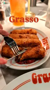 A short, punchy reel showcasing a visit to Grasso in Soho, London. The video features a quick tour of the entrance, a look at the menu, and close-up shots of popular dishes including mozzarella sticks, a vodka sauce pizza, and chicken parm with spaghetti, ending with a glimpse of the venue's 'disco' area.