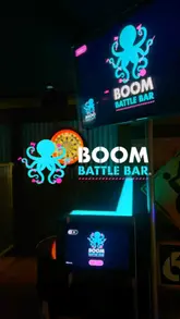 A promotional montage showcasing the activities and atmosphere at Boom Battle Bar, featuring shots of pool, darts, mini golf, and axe throwing, alongside casual bar food and cocktails.