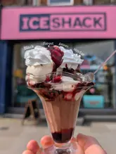 A close-up, eye-level shot of a Black Forest Gateau Sundae held in front of the Ice Shack storefront, with the venue's branding visible in the background.