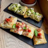 A high-quality, appetizing close-up shot of two different types of Roman-style pizza al taglio served on slate boards. The lighting is natural and flattering, highlighting the textures of the dough, cheese, and toppings.