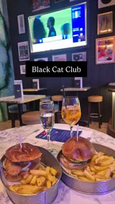 The video features a creator visiting the Black Cat Club for their Soccer Saturday bottomless brunch. It highlights the interactive bingo scorecard, the bottomless drinks, and the food (burger and fries) while explaining that the experience is enjoyable even for those not typically interested in football.