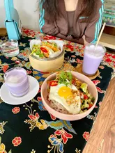 A flat-lay photograph capturing a Filipino lunch spread including a tocilog bowl, bao buns, and ube lattes, set against a highly patterned tablecloth.