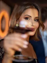 A portrait-style shot taken at an intimate omakase counter, featuring a diner holding a glass of wine in the foreground with a soft-focus background.