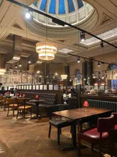 A wide-angle interior shot of the Miller & Carter Steakhouse in Glasgow, showcasing the restaurant's grand, high-ceilinged architecture and warm, moody dining atmosphere.