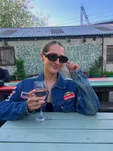 A candid, lifestyle-focused shot of a person enjoying a glass of wine in an outdoor beer garden setting. The image captures a relaxed, social atmosphere, highlighting the venue's casual, sun-drenched environment.