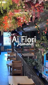 A montage showcasing the interior and food of Ai Fiori, an Italian restaurant. The video highlights the wood-fired pizza oven, the industrial-chic decor with foliage, and various dishes including pizzas and sharing platters.