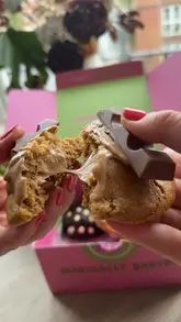 A short, punchy video showcasing a box of 'New York style' cookies from Enchanted Cookies. The video features close-up, slow-motion shots of the cookies being broken in half to reveal their gooey, filled centers, set to music with text overlays identifying the flavors.
