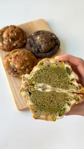 A series of high-quality, close-up shots featuring various cookies being broken in half to reveal their soft, filled centers, showcasing textures like pistachio and chocolate.