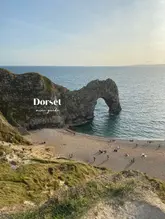 A high-quality, well-composed landscape photograph of the iconic Durdle Door arch in Dorset, used as a cover image for a travel guide. The image captures the scene during golden hour, providing warm, inviting lighting that highlights the natural beauty of the coastline.