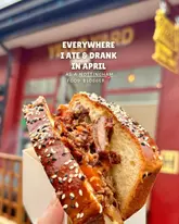 A high-quality, appetizing close-up shot of a loaded sandwich, likely taken at a street food venue. The image uses a shallow depth of field to isolate the subject against a blurred background, effectively drawing the viewer's eye to the food.