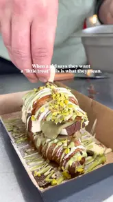 A short, punchy video showing the preparation and consumption of a pistachio and chocolate-filled croissant at a dessert stall. The video focuses on the indulgent nature of the treat, using close-up shots to highlight the textures and ingredients.
