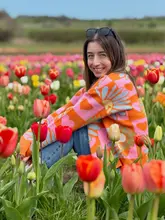 A bright, well-composed portrait of a woman sitting in a tulip field, used to promote a seasonal farm activity.
