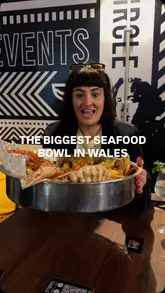 A review of Rock & Scallop in Swansea, featuring a large seafood platter with spider crab, scallops, and prawns. The video highlights the hands-on, messy nature of the meal, complete with bibs and gloves, in a lively venue setting.