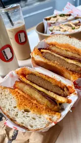 A short-form video review of a new sandwich shop in Newcastle called Breadwin. The creator showcases the interior, the ordering process, and several menu items including a breakfast bun, a pastrami sandwich, iced drinks, and pastries. The video uses a fast-paced, vlog-style format with voiceover and text overlays to highlight the food quality and venue atmosphere.