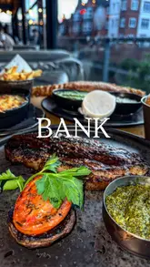 A promotional video for 'Bank' restaurant in Birmingham, showcasing a variety of dishes including steak, fish and chips, and mac and cheese, alongside shots of the restaurant's interior and exterior.