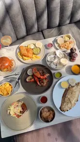 A high-quality montage showcasing a seafood restaurant in Borough Market, featuring close-ups of various dishes like lobster, oysters, and fish and chips, alongside shots of the kitchen and the venue's interior and exterior views.