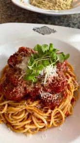A video review of a family-run Italian restaurant, featuring close-ups of new menu items like whitebait, pistachio spaghetti with burrata, and meatball pasta, alongside a pizza and side dishes. The creator captures the dining experience, including the service and the restaurant's atmosphere.