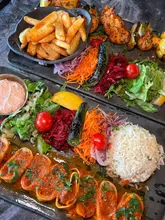 A top-down, overhead shot of two Turkish main courses, featuring lamb sarma beyti and monkfish kebab, served with rice, salad, and fries on large rectangular platters.