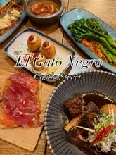 A flat-lay overhead shot of a table filled with various tapas dishes at El Gato Negro, featuring text overlay identifying the venue.