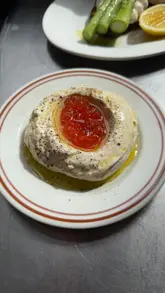 The video features a chef demonstrating how to prepare taramasalata using cured and smoked cod roe. The creator walks the viewer through the process, from selecting the roe to blending the ingredients and plating the final dish with grilled bread and asparagus.