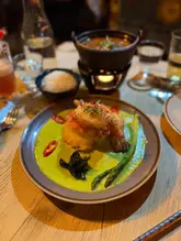 A close-up, eye-level shot of a king river prawn green curry dish served in a restaurant setting, featuring a vibrant green sauce and crispy prawn garnish.