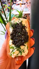 A short, fast-paced review of a unique 'caviar cream cheese hot dog' and accompanying sides at a London food market stall. The video features close-up shots of the food, including truffle fries, pork belly bites, and a caviar caramel sundae, interspersed with brief glimpses of the venue's interior.