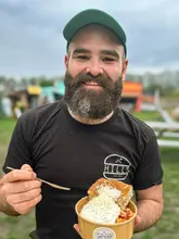 A portrait of a man holding a bowl of pasta topped with burrata and parmesan at an outdoor market event.