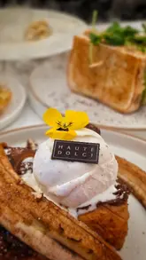 A montage video showcasing various food and drink items from Haute Dolci, including a milkshake, french toast, a club sandwich, truffle pasta, and a large chocolate cake.