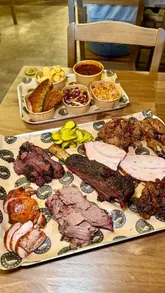 A short, punchy montage showcasing a meat platter, smash burger, and desserts at Tea's Smokehouse. The video focuses on close-up shots of the food, highlighting the texture and quality of the smoked meats, before ending with a brief shot of the venue's counter.