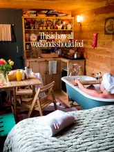 A cozy, inviting lifestyle shot of a glamping cabin interior, featuring a person relaxing in a bathtub with a book and a drink. The warm lighting and rustic decor create a strong sense of atmosphere and escapism, effectively selling the experience of a relaxing getaway.