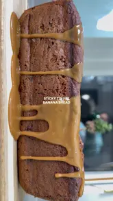 A high-quality, close-up food video demonstrating the finishing touches of a sticky toffee banana bread, featuring slow-motion pours of toffee sauce and cream, followed by slicing and stacking.