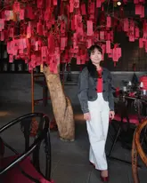 A portrait of a creator standing in the dining room of a high-end Chinese restaurant, positioned in front of a decorative wishing tree with red tags. The image captures the interior aesthetic of the venue.
