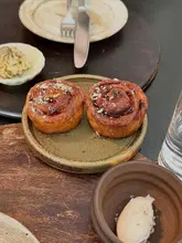 A high-quality, close-up shot of two glazed pastries served on a rustic ceramic plate, likely at a fine dining establishment. The composition is clean, with a shallow depth of field that highlights the texture of the pastries while providing context with a table setting in the background.