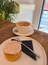 A simple, natural-light shot of a coffee and a cinnamon roll served on a wooden table, likely in a cafe.