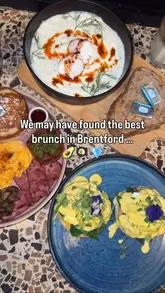A short review video of a brunch spot in Brentford called Rada Coffee & Eatery. The video features close-up shots of various brunch dishes including Turkish eggs, a full English breakfast, and pistachio French toast, along with an iced latte. The creators are shown enjoying the food, and the video concludes with a brief shot of the cafe interior.