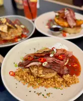 A close-up, slightly angled shot of three brunch plates featuring loaded crumpets topped with ingredients like bacon, halloumi, poached eggs, and chilli jam, set against a dark table surface.