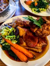 A high-quality, appetizing close-up shot of a traditional Sunday roast dinner, featuring perfectly cooked sirloin of beef, a golden Yorkshire pudding, and vibrant vegetables. The lighting is soft and natural, highlighting the textures of the food, while the shallow depth of field keeps the focus squarely on the main plate.