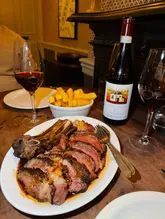 A dimly lit, atmospheric shot of a prime rib steak dinner accompanied by a bottle of Barolo and red wine, capturing a classic date-night steakhouse vibe.