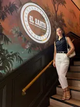 A high-quality, well-composed lifestyle shot of a woman posing on a staircase in front of an illuminated 'El Santo' sign, effectively showcasing the venue's interior design and atmosphere for a date night setting.