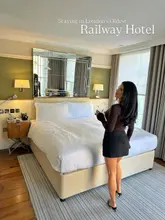 A high-quality, well-lit photograph featuring a creator standing in a hotel room, showcasing the interior design and atmosphere of what is identified as London's oldest railway hotel. The image is clean, professional, and effectively communicates a travel and lifestyle experience.