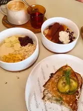 A bright, overhead flat-lay shot of a brunch spread at a cafe, featuring two bowls of porridge, a smoked salmon toastie, and two drinks, arranged neatly on a table.