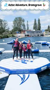A fast-paced video showcasing an inflatable aqua park obstacle course on a lake. The footage includes drone shots of the entire setup and handheld action shots of people climbing, jumping, and falling into the water, highlighting the fun and active nature of the venue.