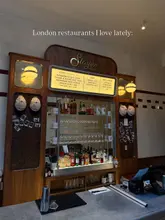 A clean, symmetrical, and well-lit wide shot of the bar area at Slayer Pizzeria, showcasing the menu board, spirit selection, and interior branding.