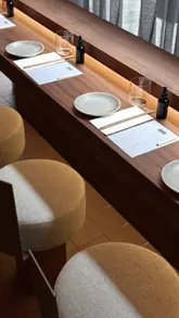 A short, aesthetic video showcasing a modern, dimly lit sushi bar. The footage highlights the counter seating, chefs preparing food, and close-ups of handrolls and sashimi, set to music with minimal text overlay.