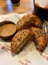 A close-up, top-down shot of prawn toast crumpets served with a dipping sauce on branded paper, likely taken at a casual dining venue.