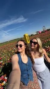 The video is a montage of a day out at Farmer Copleys, featuring shots of tulip fields, the farm shop, ice cream, and a milk vending machine, followed by a visit to a botanical garden. It captures a relaxed, aesthetic 'girly day' vibe.